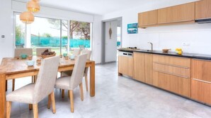 A modern kitchen with wooden cabinets, a black countertop, and a dining area with a wooden table and chairs. - Almendro by Interhome (Sta Cristina d'Aro)