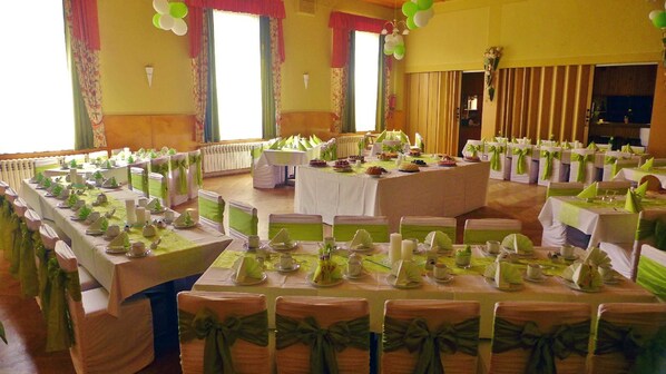A banquet hall with multiple round tables set for a formal event, featuring green and white tablecloths and matching chair sashes.