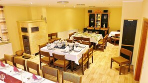 A dining area with multiple tables set for a meal, wooden chairs, and a cabinet with kitchenware.