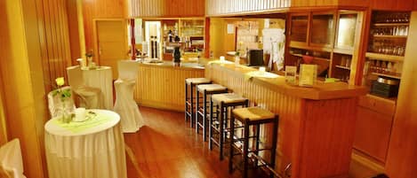 Zona de bar con paneles de madera, una barra con taburetes y estanterías llenas de vasos y botellas.