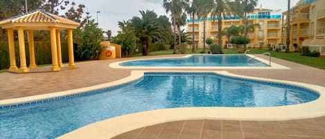 Une piscine au design incurvé, un kiosque et un bâtiment doté de balcons.