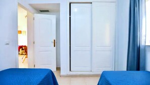 Una stanza con due letti, un armadio e una porta che dà su un'altra stanza.