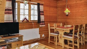 A cozy wooden cabin interior with a television, wooden dining table, chairs, and a hanging lamp.