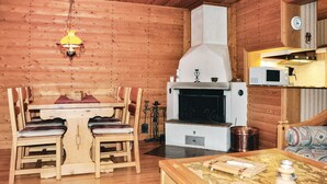 A cozy wooden cabin interior with a dining table, chairs, a fireplace, a hanging light fixture, and a microwave.