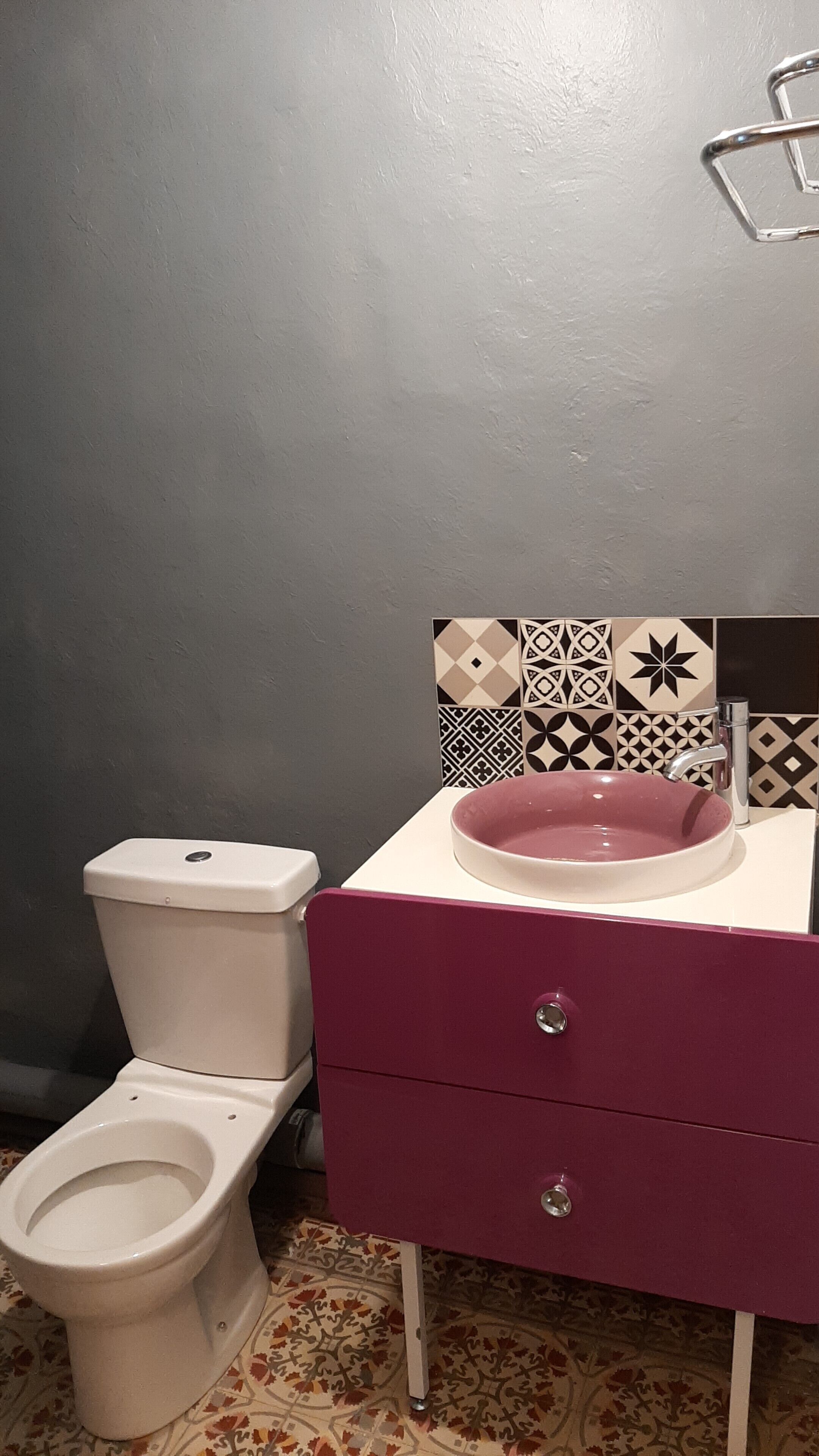 A bathroom with a white toilet, a pink sink, and a vanity with a patterned tile backsplash.