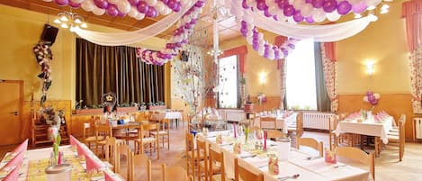 Un salón de banquetes con varias mesas redondas, cada una cubierta con manteles blancos, servilletas rosas y cubiertos.