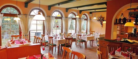 A dining area with multiple tables, chairs, and hanging lamps.