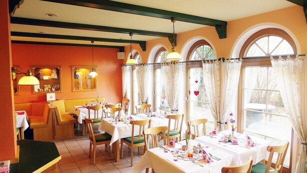 Un restaurante con varias mesas y sillas, amplias ventanas con cortinas, y una decoración con colores cálidos.