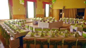 Un salón de banquetes con varias mesas redondas dispuestas para un evento formal, con manteles y lazos de sillas blancos y verdes.