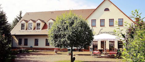 Un bâtiment traditionnel avec un toit en tuiles, un arbre au centre et des tables à l’extérieur pour un restaurant.