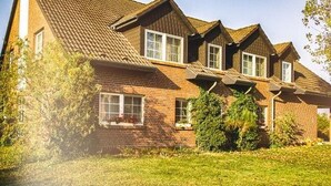 Una casa de dues plantes amb teulada inclinada, parets de maó i diverses finestres.
