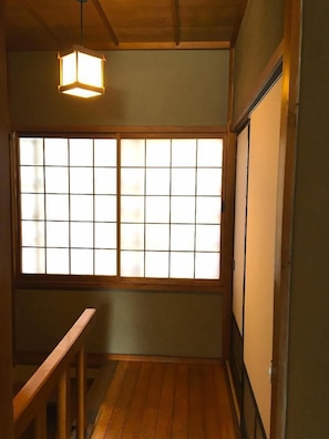 A room with a wooden floor, a window with a grid pattern, and a hanging light fixture.