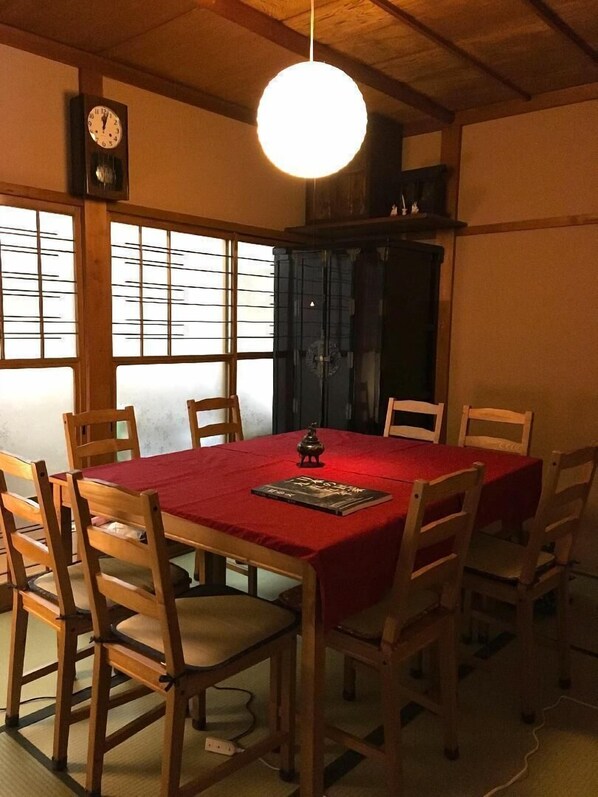A dining room with a wooden table and chairs, a red tablecloth, a clock on the wall, and a hanging light fixture.