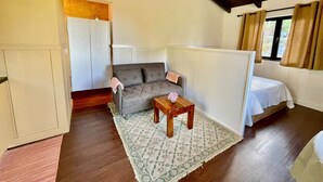 Una habitació acollidora amb un sofà, una taula petita amb un ram i un llit, i una finestra amb cortines.