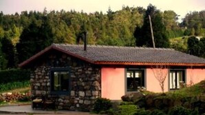 Una casa de pedra amb teulada vermella, envoltada de vegetació i un turó boscos