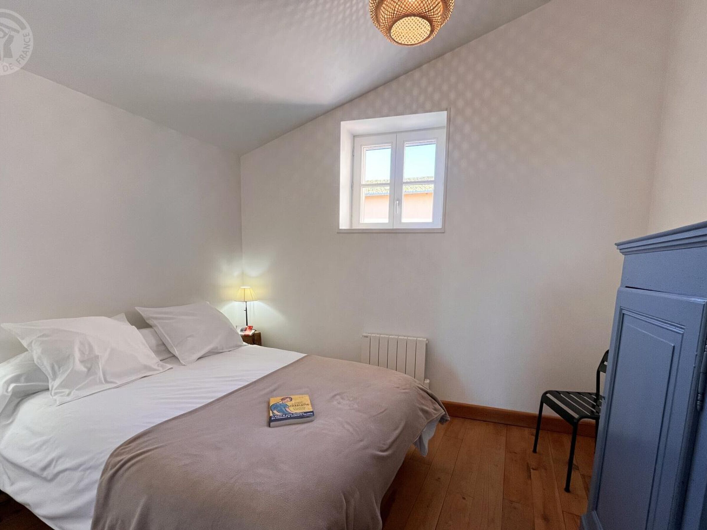 A bedroom with a bed, a nightstand with a lamp, a radiator, a window, and a wardrobe.
