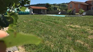 A grassy backyard with a swimming pool, a small shed, and two houses with red roofs. - Cozy getaway with garden and Wi-Fi, romantic retreat (Saint-André-d'Apchon)
