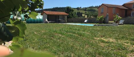Un patio trasero con césped, una piscina, un cobertizo pequeño y dos casas con tejados rojos.