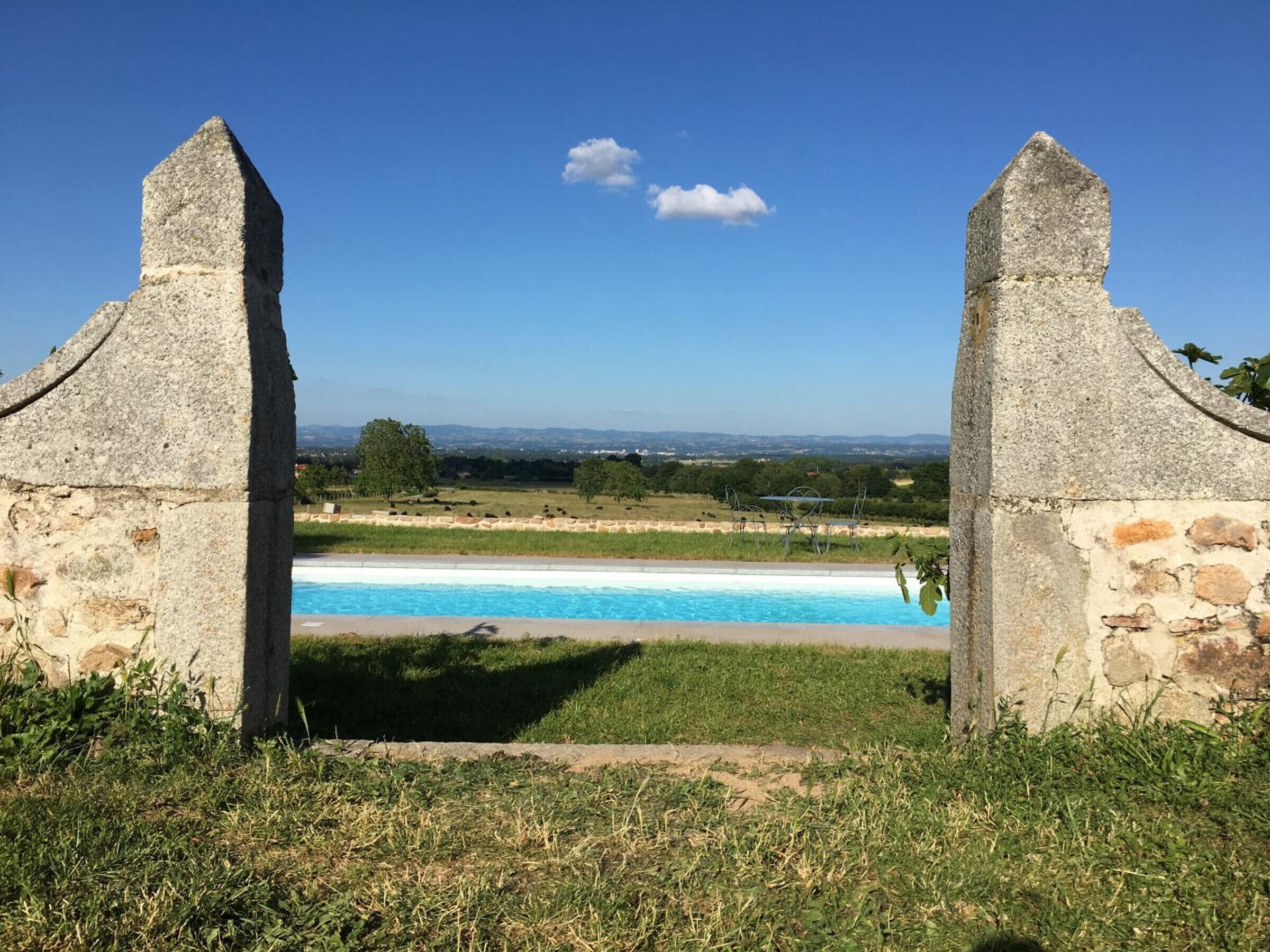 Un arc en pierre mène à une piscine d’où l’on peut admirer des collines et des arbres au loin.
