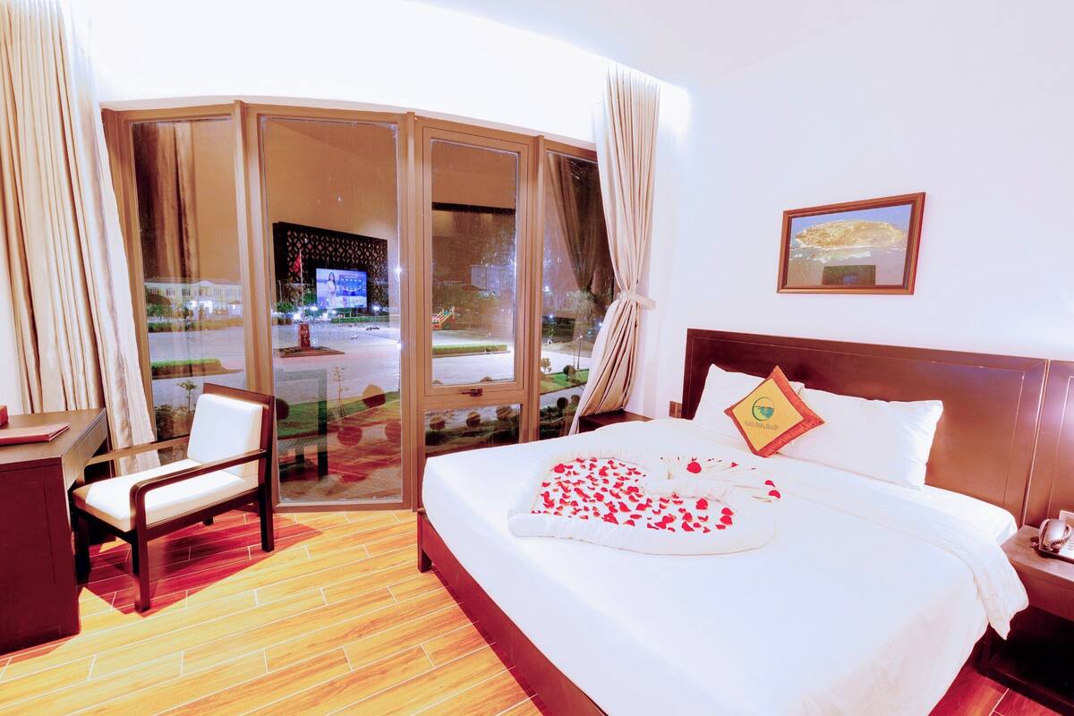 A hotel room with a large bed, a chair, a desk, and a view of the outside.