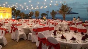 Un salón de banquetes con mesas redondas dispuestas para un evento formal, decorado con manteles blancos y fajas rojas.