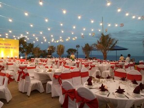 A banquet hall with round tables set for a formal event, decorated with white tablecloths and red sashes.