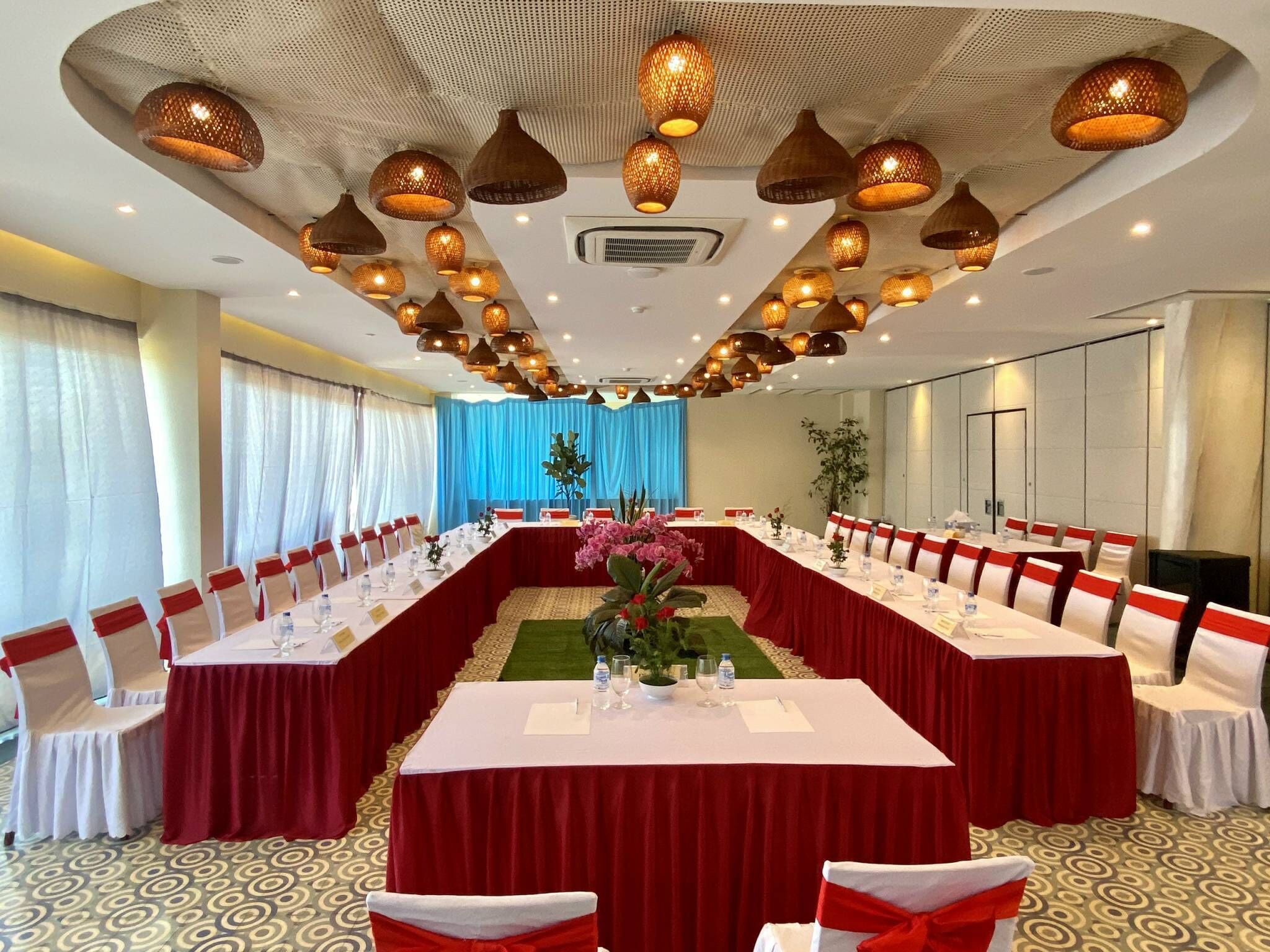 A conference room with a long table, red and white chairs, and decorative hanging lights.
