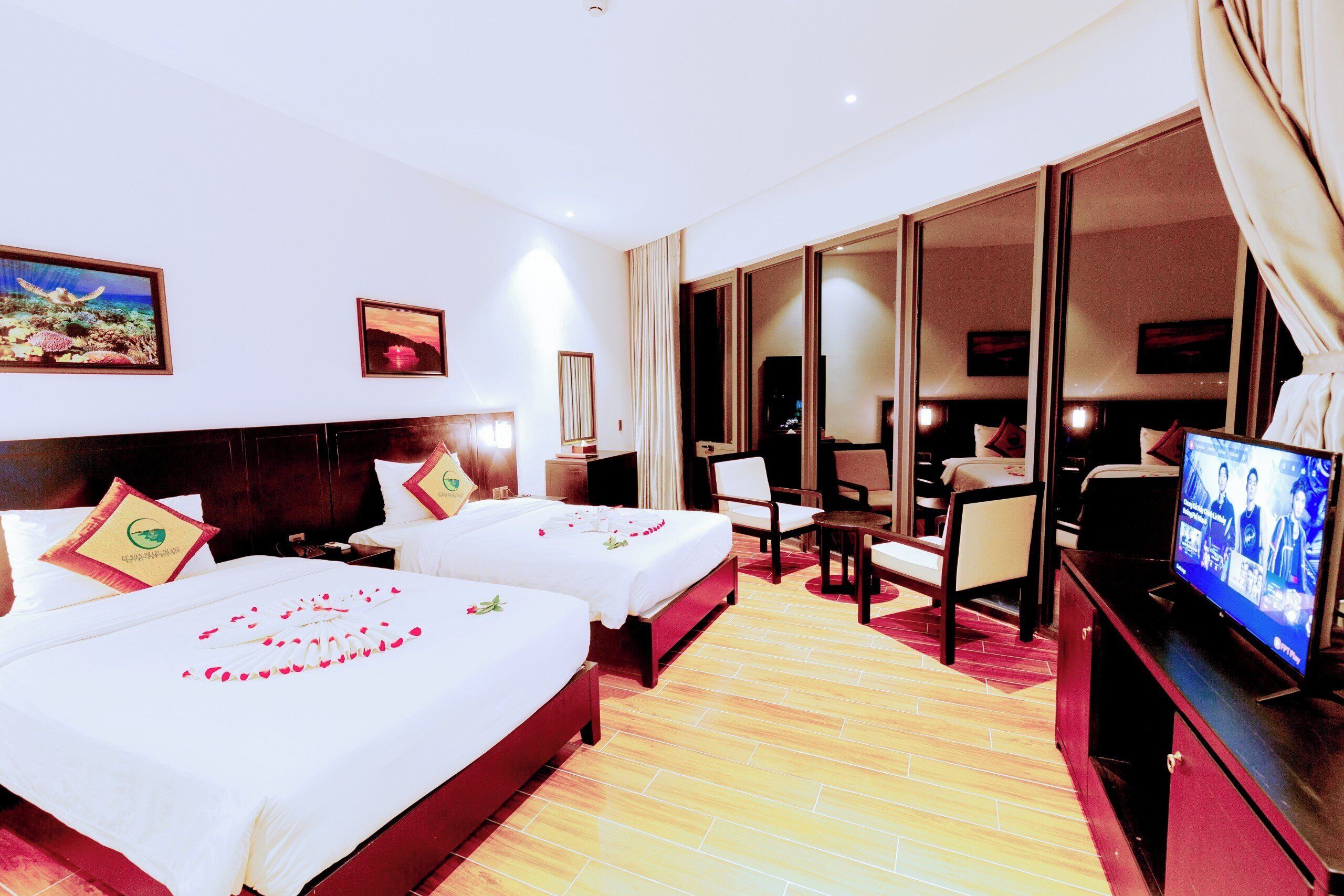 Habitación de hotel con dos camas, televisión, escritorio y un ventanal grande.