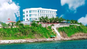 Un hotel blanco de varios pisos con una escalera que conduce a los niveles superiores, ubicado en un acantilado costero con vista al mar.