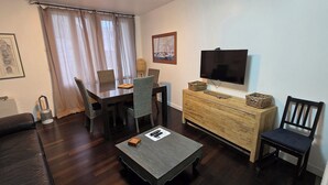 Un salon meublé comprenant une table à manger, des chaises, un canapé, une table basse, un téléviseur et un meuble en bois.