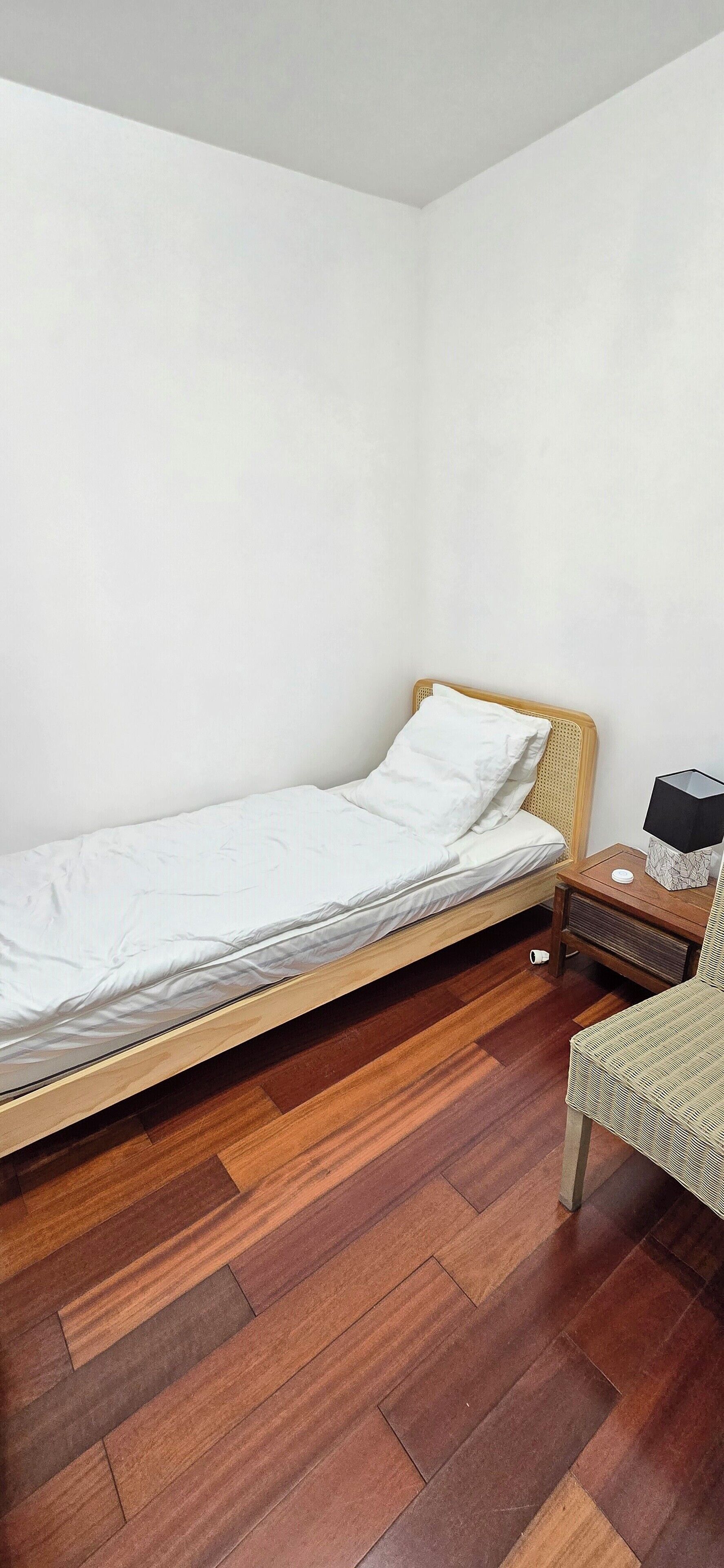 Habitació petita amb un llit individual, sòl de fusta i una petita taula de nit.