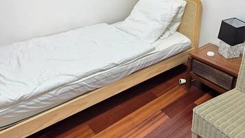 Habitació petita amb un llit individual, sòl de fusta i una petita taula de nit.