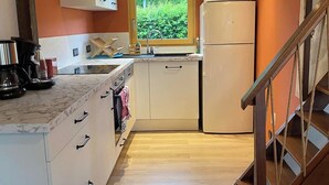 A compact kitchen with white cabinets, a built-in microwave, and a wooden staircase.