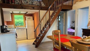 A cozy kitchen with wooden cabinets, a built-in microwave, and a refrigerator. A wooden staircase leads to a dining area with a table and chairs.
