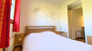 Een slaapkamer met een houten hoofdeinde, twee wanddecoraties van vlinders, een nachtkastje met een lamp en een raam met rode gordijnen.