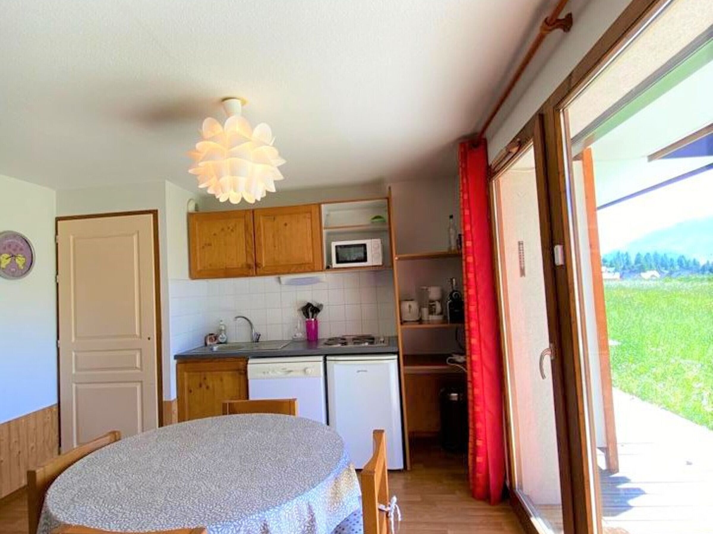 A compact kitchen with wooden cabinets, a microwave, and a sink. There's a dining table with a patterned tablecloth.