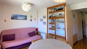Een knusse woonkamer met een roze gestreepte bank, een houten kast met planken, en een ronde tafel.