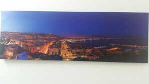 Vista panorámica de una ciudad costera de noche, con edificios iluminados y un puente a lo lejos.
