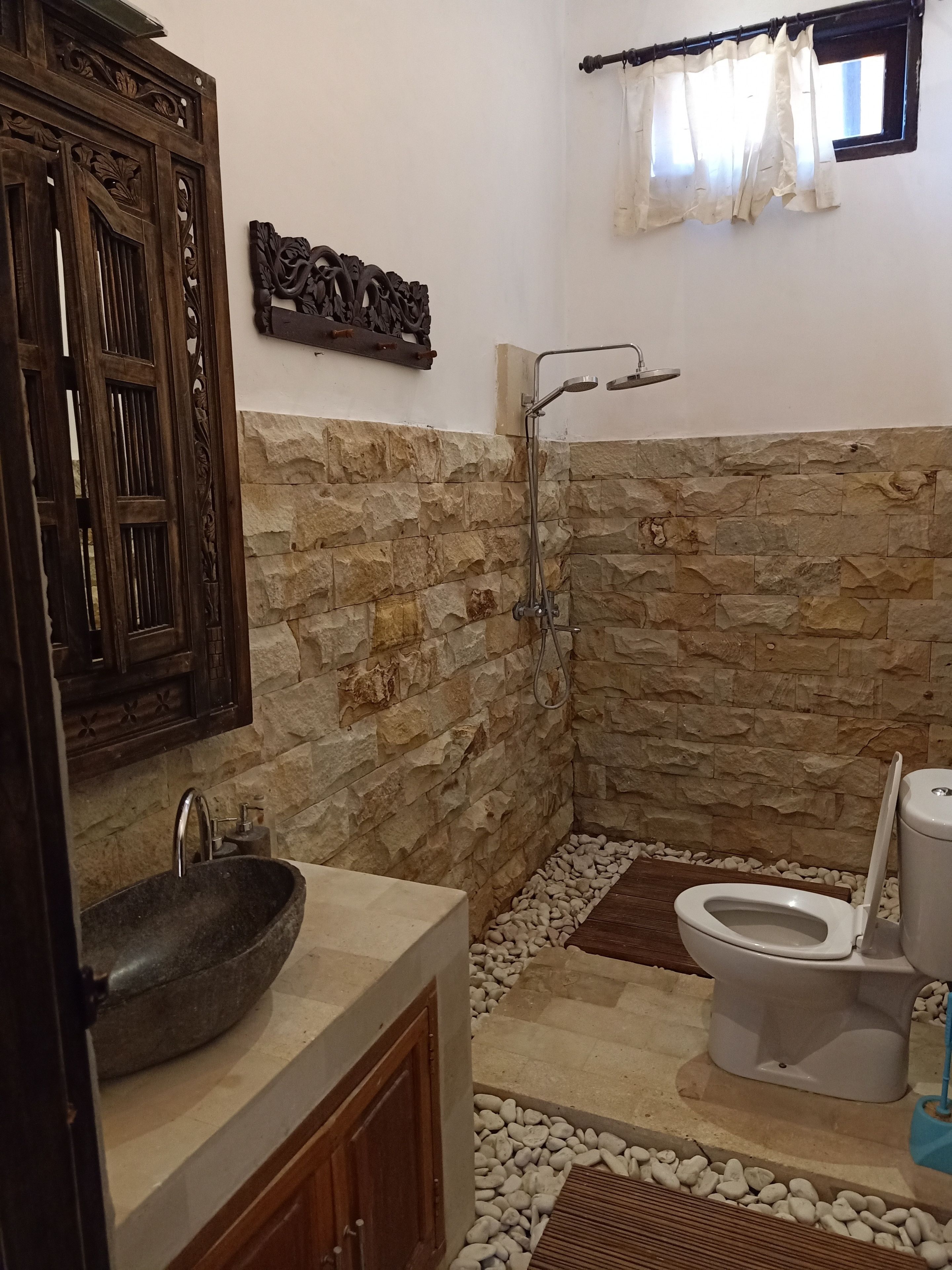 A bathroom with a stone wall, a wooden cabinet, a sink, a toilet, and a shower.