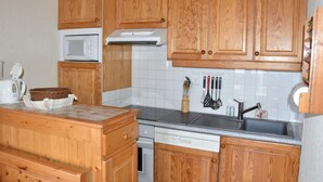 Uma cozinha com armários de madeira, micro-ondas, lava-louças e diversos utensílios sobre o balcão.