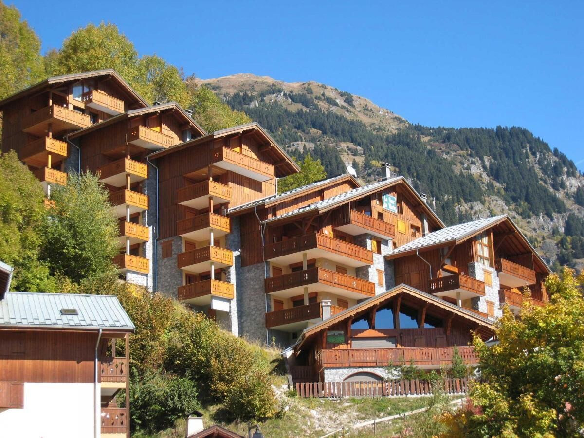 A multi-story wooden chalet with balconies, set against a mountainous backdrop.