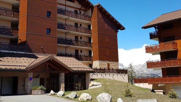A multi-story hotel with balconies, a stone facade, and a mountainous backdrop. - Studio cabin 4 pers, mountain view, ski access (La Joue du Loup)