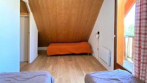 Una habitación pequeña y acogedora con techos inclinados de madera, dos camas individuales y una ventana con vistas al exterior.