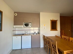 A compact kitchen with a microwave, a small refrigerator, a dishwasher, and a dining table with chairs.
