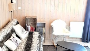 A cozy living room with a wooden wall, a sofa with patterned cushions, a white chair, and a bookshelf.