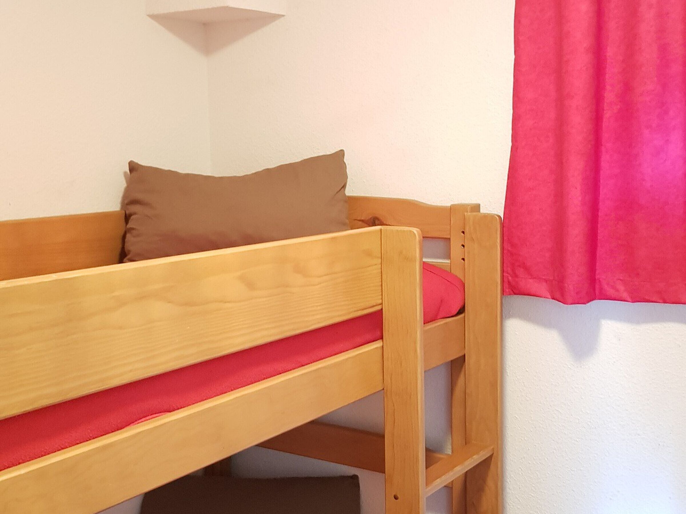 A wooden bunk bed with a red mattress and a brown pillow.