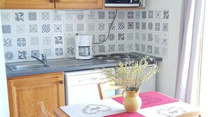A kitchen with patterned tiles, a coffee maker, a stove, and a dining table with a vase of flowers. - Studio cabin La Joue du Loup, 4 ppl., terrace, parking (La Joue du Loup)