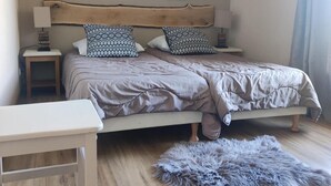 A bedroom with a wooden headboard, two bedside tables with lamps, patterned pillows, a bed with a grey duvet, a small white bedside table, and a fluffy grey rug.