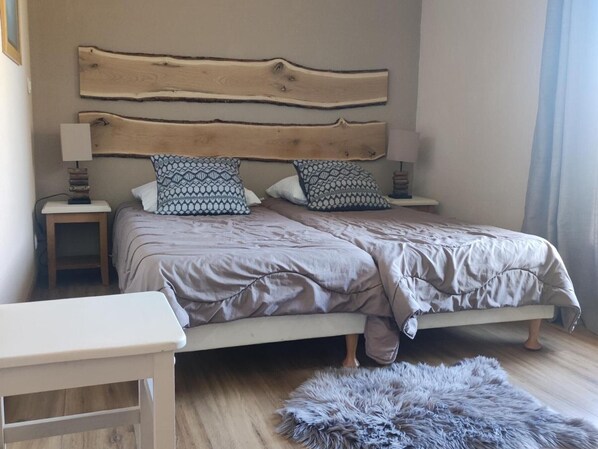 A bedroom with a wooden headboard, two bedside tables with lamps, patterned pillows, a bed with a grey duvet, a small white bedside table, and a fluffy grey rug. - Duplex chalet 3 rooms for 7 pers. with terrace and free parking (La Joue du Loup)
