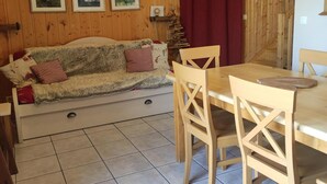 A wooden interior with a sofa, dining table, chairs, and framed pictures on the wall.